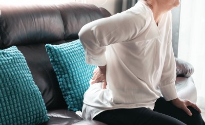 Woman leaning forward on couch with hand on lower back